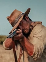 Brandon Sklenar as Spencer Dutton in brown safari fedora aiming double-barrel rifle in 1923 action scene arid landscape