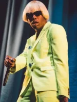 Tyler the Creator performing on stage in lime green Igor suit with blond wig and sunglasses on blue curtain backdrop