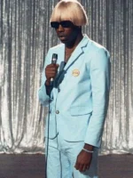 Tyler the Creator wearing Igor blue suit with blond wig and sunglasses performing with microphone on silver curtain stage