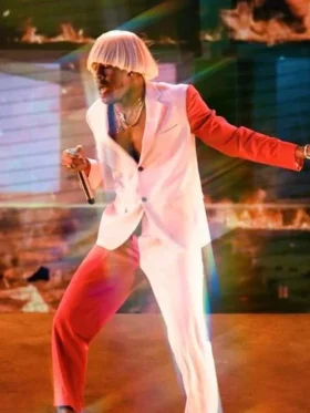 Tyler the Creator performing on stage in pink Igor blazer with red trousers and blond wig in dynamic performance pose