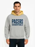 Front view of a man wearing the Fear of God Essentials NBA Pacers hoodie in heather grey, featuring a contrasting yellow hood, blue "Pacers Essentials" chest print, a kangaroo pocket, and an NBA logo on the left sleeve cuff.