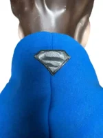 A close-up view of the upper hood section on the blue Youngla Superman hoodie. The shot details a small, premium metallic black and silver embroidered Superman shield patch seamlessly stitched onto the center-back seam of the blue fabric.