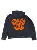 A close-up of a black denim jacket chest pocket with a small, raised black-thread embroidery of a Mickey Mouse-shaped jack-o'-lantern.