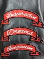 A black Amiri varsity jacket featuring leather sleeves, embroidered logo patches, and a rib-knitted collar.