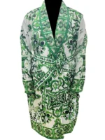 Nick Jonas standing in a lavishly decorated living room wearing a plush, dark green velvet robe with gold embroidery