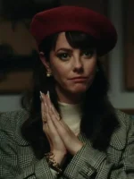 Close-up of Kaya Scodelario in a tartan trench coat and red beret, wearing a luxurious plaid coat with pearl earrings.