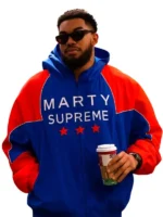Detailed close-up of the royal blue and orange Marty Supreme jacket texture and patches.