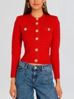 A front view of Ashley Park as Mindy Chen wearing a red Retrofete knitted jacket with gold button embellishments.