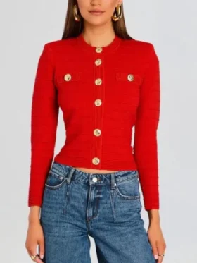 A front view of Ashley Park as Mindy Chen wearing a red Retrofete knitted jacket with gold button embellishments.