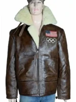 Front view of the 2026 Winter Olympics Team USA brown leather flight jacket displayed on a male mannequin. The B-3 style aviator jacket features a heavily textured brown distressed leather shell, an oversized cream-colored plush shearling collar with throat latch straps, a full-length front zipper, and spacious side patch pockets. The left chest is adorned with an embroidered United States flag patch situated directly above the iconic white Olympic rings logo.