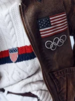 Close-up of the American flag and Olympic Rings patches on the front of the 2026 Team USA flight jacket.