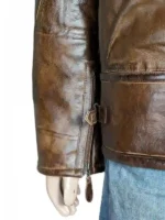 A close-up side view of the sleeve and lower torso of the 2026 Winter Olympics Team USA brown leather flight jacket. The shot details the heavily distressed, rugged grain texture of the brown leather hide. It highlights a heavy-duty vertical wrist zipper closure at the cuff with a leather pull tab, alongside an adjustable waist strap with a metal buckle located near the lower side seam.