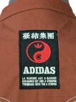 The Adidas x CLOT Chinese New Year track jacket in Fox Brown on a mannequin stand, detailing the Western deco back stitching and white sleeve stripes.