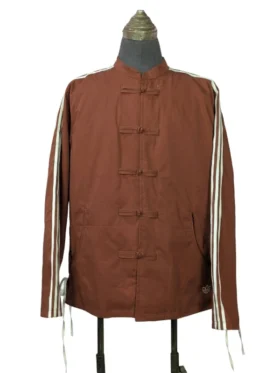 A studio product shot of a male model wearing the full-zip Adidas x CLOT Chinese New Year track jacket in Fox Brown, featuring a mandarin collar with traditional white frog closures over a silver zipper and white rope three-stripes down the sleeves.