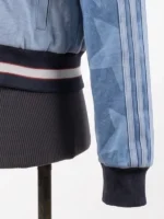 Close-up of a denim bomber jacket's sleeve showing an all-over star graphic print, three-stripe piping, and a ribbed knit cuff and waistband.