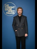Studio portrait of Ryan Gosling wearing a charcoal grey wool cashmere double breasted jacket in front of The Tonight Show backdrop.
