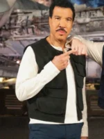 Lionel Richie pointing while wearing a black cotton vest over a white shirt in a stage background