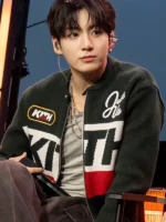 Jungkook in black Kith varsity knit jacket with white red colorblock and KITH branding seated at BTS Swimside Event 2026