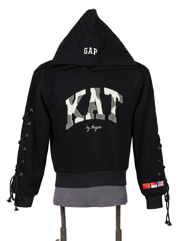 Front view of a black pullover fleece hoodie on a mannequin featuring large camo varsity lettering across the chest and decorative lace-up sleeve details.