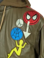 A detailed close-up shot of the four custom pop-art chest patches on the Peter Parker Photographer jacket, displaying a red Spider-Man emblem, a white peace sign, a blue web graphic, and a yellow stick figure.