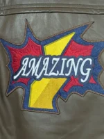 A detailed close-up shot of the large comic-style "AMAZING" patch on the back of the olive green Peter Parker Photographer jacket, displaying embroidered yellow, red, blue, and white thread textures.