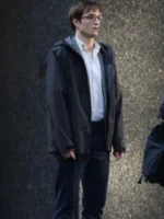 Side profile of Robert Pattinson wearing a black hooded jacket over a white shirt with dark trousers in an outdoor setting