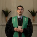 Dan Levy wearing green and black pastor robes as the character Nicky in the Netflix series Big Mistakes.