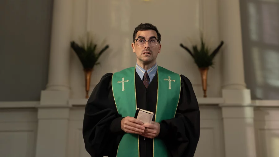 Dan Levy wearing green and black pastor robes as the character Nicky in the Netflix series Big Mistakes.