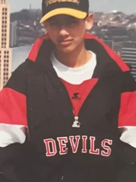 Full childhood photo of young Sunny Mehta wearing New Jersey Devils Starter jacket with Devils cap in front of New York City skyline