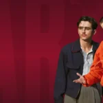 Three male models wearing Marty Supreme jackets including orange Marty Supreme windbreaker, navy jacket and black suit at TVJackets