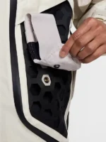 Hand detaching modular snap pocket from Nike ISPA Butterfly Jacket Orewood Brown showing brass snap button and black hexagon rubber grid panel