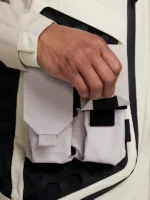 Hand configuring velcro modular pocket unit on Nike ISPA Butterfly Jacket Orewood Brown against black hexagonal rubber grid panel