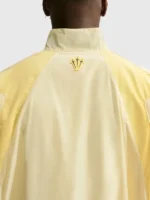Back view of NOCTA Northstar Yellow Track Jacket with yellow polyester fabric, stand collar, and elastic hem