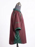 Side profile view of the maroon CJ x Nike Portugal Total 90 Retro Jersey on a mannequin, showcasing green airbrush detailing under the arm and graphics on the sleeve.