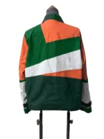 Rear view of a color-blocked windbreaker jacket on a mannequin displaying large angular patches of orange, emerald green, white, and deep green.