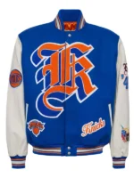 Front view of a royal blue and cream New York Knicks varsity jacket featuring bold gothic letter embroidery, team patches, and striped ribbed trim.
